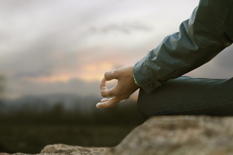 An image of the hand of a young man at the top of the mountain at sunrise, practicing meditation after he learn how to manage anxiety, start online therapy for anxiety with Foram Zaveri Therapy